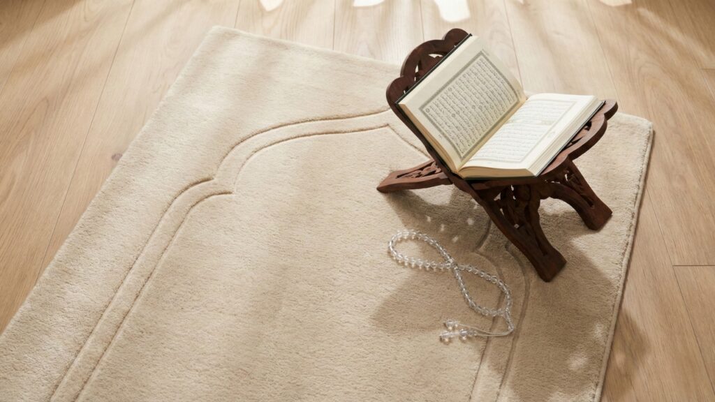 Minimalist memory foam prayer mat in beige with wooden Quran stand and prayer beads.