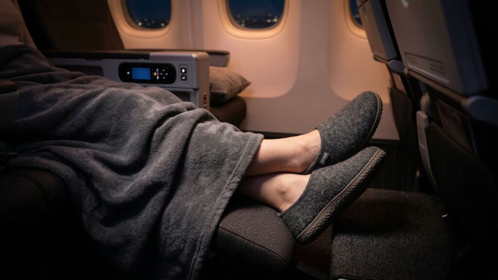 Passenger resting comfortably in an airplane seat wearing cozy Greys Outdoor Slippers during a long flight.